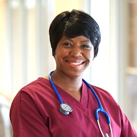 Enfermera sonriente con ropa quirúrgica color borgoña con un estetoscopio 3M Littmann Classic III con tubos azules.